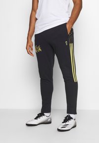 Svarta träningsbyxor med gula ränder, med en grafisk logotyp i guld på vänster lår och en åtsittande design. Kombinera med fotbollsskor.