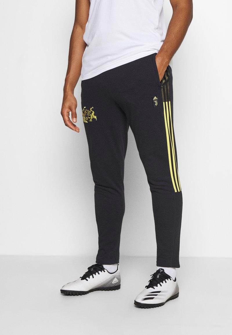 Svarta träningsbyxor med gula ränder, med en grafisk logotyp i guld på vänster lår och en åtsittande design. Kombinera med fotbollsskor.