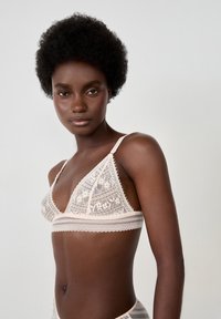 Lace bralette in soft beige with triangular cups, floral patterns, adjustable straps, and a delicate scalloped trim.