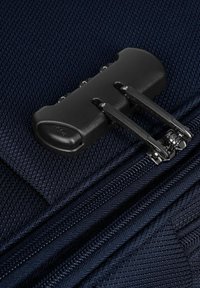 Tirante della cerniera nera con due punte di metallo, in contrasto con uno sfondo di tessuto texturizzato blu scuro. Presenta una parte superiore arrotondata e un funzionamento fluido.