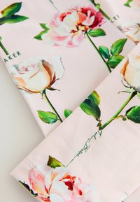 Fabric with a light pink background featuring printed large white and pink roses with green leaves and stems.