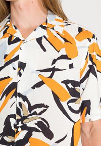 Short-sleeve shirt in lightweight fabric, featuring a bold abstract pattern of orange, black, and gray on a white background. Buttoned collar.