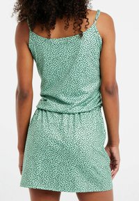 Robe verte sans manches à pois noirs, taille cintrée et ourlet droit. Tissu lisse et léger avec bretelles réglables.