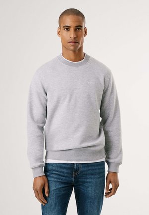 Gray crewneck sweatshirt in soft fabric with ribbed cuffs and hem; features subtle logo embroidery on the chest. Worn with blue jeans.