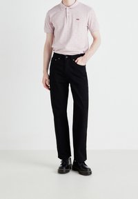 Světle růžová polo košile s malými tmavými tečkami, spárovaná s černými džíny rovného střihu a černými botami s žlutým prošitím.