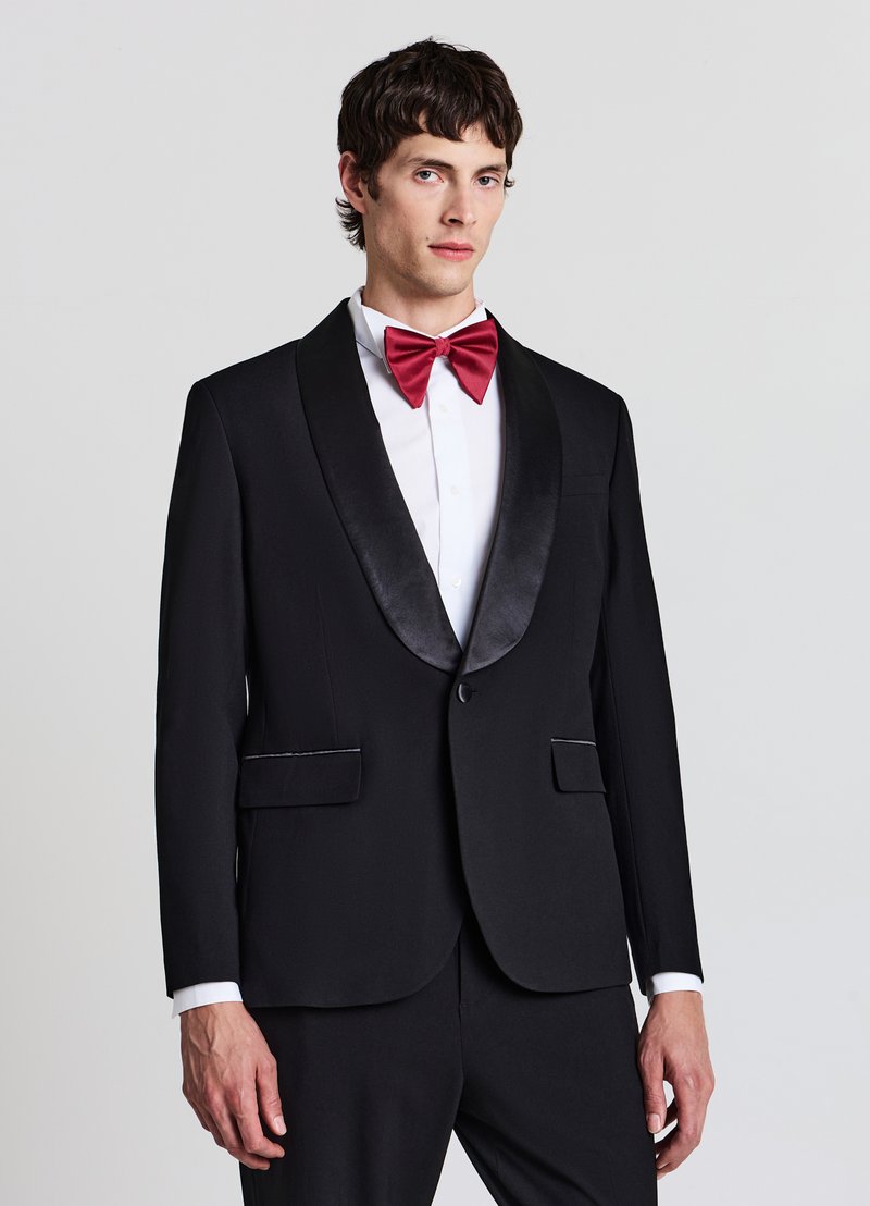 Giacca da smoking nera con rever in raso, pantaloni abbinati, camicia bianca e papillon rosso. Tessuto liscio con design strutturato e tasche.