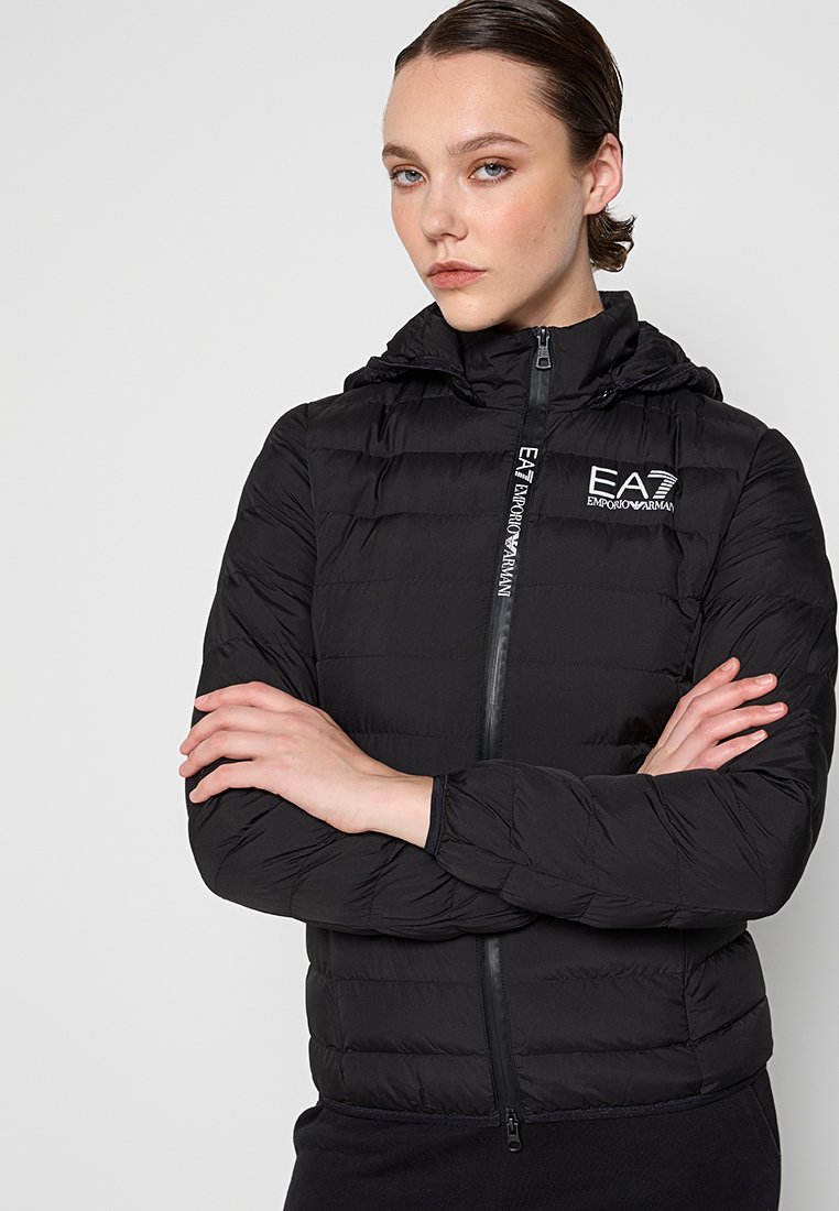 Czarna kurtka puchowa z kapturem, z zamkiem błyskawicznym i pikowanym wzorem. Zawiera logo EA7 po lewej stronie klatki piersiowej i gładką fakturę.