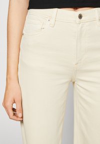 Beiga vida jeans i denim, med framfickor, en metallknappstängning och subtil sömnad längs sömmarna.