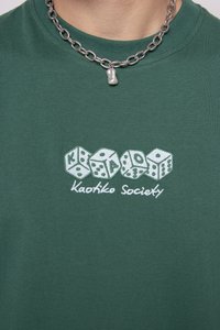 Green cotton t-shirt featuring embroidered dice graphic and text "Kaotiko Society" in white. The fabric is smooth with a crew neckline.