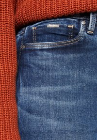 Mörkblå denimjeans har en klassisk passform med lätt slitage. Midjan har synlig sömnad och en silverfärgad knappdetalj.