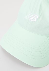 Căciulă verde mentă cu un design structurat, având un logo brodat alb și modele de cusături vizibile pe vârful acesteia.