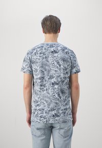 Short-sleeve t-shirt in light blue with dark blue leaf pattern; round neckline, soft fabric, and relaxed fit. Worn with denim jeans.