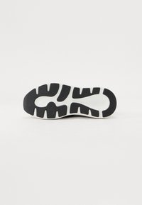 Semelle de sneaker noir et blanc présentant un caoutchouc texturé avec des rainures et des motifs, offrant adhérence et durabilité.