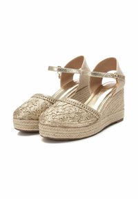 Wedge espadrillas dorate con piattaforma in juta intrecciata, parte superiore ricamata e sottili cinturini alla caviglia. Accenti metallici lisci.