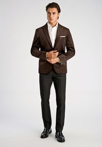 Brun mockakavaj med notchade slag, vit skjorta, svarta byxor och blanka svarta loafers. Enkel näsduk i bröstfickan.