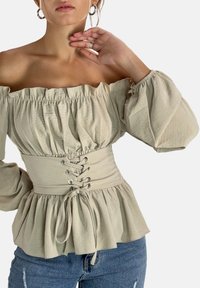 Beige Oberteil mit schulterfreiem Design, gepufften Ärmeln, tailliertem Schnürverschluss und ausgestellt geschnittenem Saum. Der Stoff hat eine weiche, strukturierte Optik.