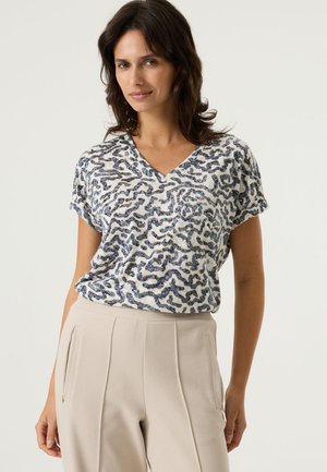 Korte mouw V-hals top met een visueel patroon in blauw en wit. Zachte stoftextuur, ontspannen pasvorm, gecombineerd met beige broek.