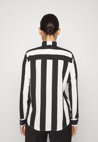 Schwarz-weißer gestreifter Langarmshirt mit einem Hemdkragen, Knopfmanschetten und einem geschwungenen Saum, gefertigt aus einem glatten Textil.