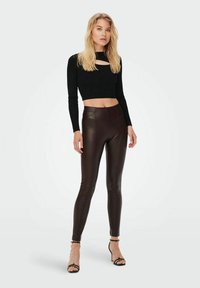 Sort croppet langærmet top med en forkant, parret med højtaljede, glansfulde brune kunstlæderleggings og strappy sorte hæle.