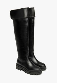Schwarze Overknee-Stiefel aus Leder mit abgerundetem Fuß, klobiger Sohle und umgeklapptem Bund an der Oberseite. Strukturierte Oberfläche.