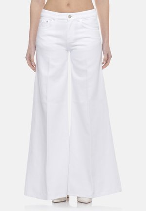 Pantaloni bianchi a gamba larga indossati da una persona in piedi, con tasche frontali visibili e chiusura con bottoni, abbinati a scarpe bianche a punta.