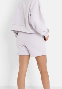 Ljust lila sweatshirt med sänkt axel, tillsammans med matchande åtsittande shorts. Mjuk tyg och minimalistisk design. Inga synliga mönster.