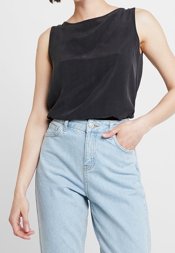 Top nero senza maniche con una texture morbida e liscia e scollatura a barca, abbinato a jeans azzurri chiari a vita alta con chiusura a bottoni classica.