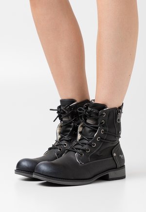 Bottes de cheville en cuir noir à lacets avec œillets en métal, doublure rembourrée, fermeture éclair latérale et accents texturés au niveau des orteils et du talon.