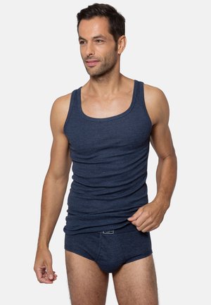 Homme portant un débardeur à côtes bleu marine assorti à un slip, se tenant contre un fond gris clair uni.