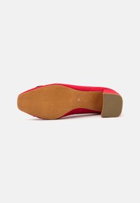 Escarpin en daim rouge avec un bout pointu, un petit talon large, et une semelle extérieure en caoutchouc brun texturé. Aucune marque ou embellissement visible.