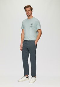 T-shirt en coton bleu clair avec un imprimé graphique, associé à un pantalon en coton gris. Chaussures : baskets blanches avec des accents bleu marine.