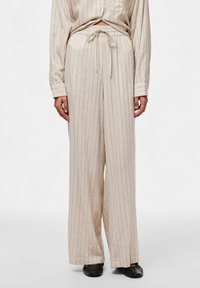 Pantalons larges rayés, de couleur beige clair, avec une taille élastique dotée d'un cordon de serrage. Tissu doux avec une coupe décontractée.