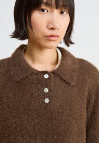 Brown fuzzy knit sweater with a large collar, featuring three decorative buttons in front. Soft texture and relaxed fit.