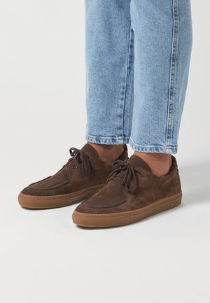Zapatillas de ante marrón con diseño de cordones, suela de goma y costura tonal. Punta redondeada y sutiles acentos de costura en la parte superior.
