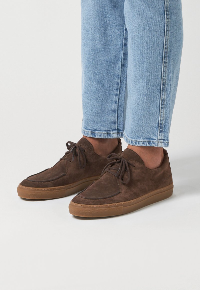 Baskets en daim marron avec un design à lacets, semelle en caoutchouc et coutures tonales. Embout arrondi et accents de couture subtils sur la tige.