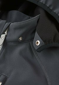 Giacca resistente all'acqua con un'esterno grigio scuro, morbida fodera in pile nero, chiusure a scatto e con cerniera, e dettagli di cuciture rinforzate.