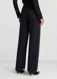 Schwarz hoch taillierte Jeans aus Denim mit weitem Bein, minimaler Nahtführung und glatter Textur. Kombiniert mit schwarzen Absatzschuhen.