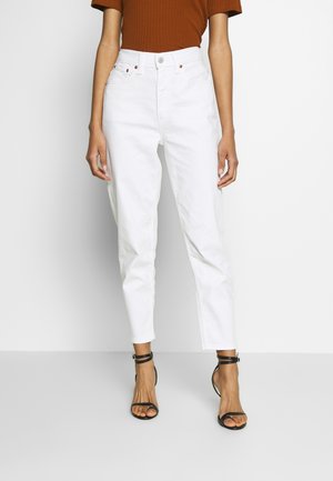 Jeans bianchi a vita alta con silhouette a gamba affusolata, dotati di chiusura con bottone frontale e cinque tasche. Abbinati a un top brown a coste e sandali neri.