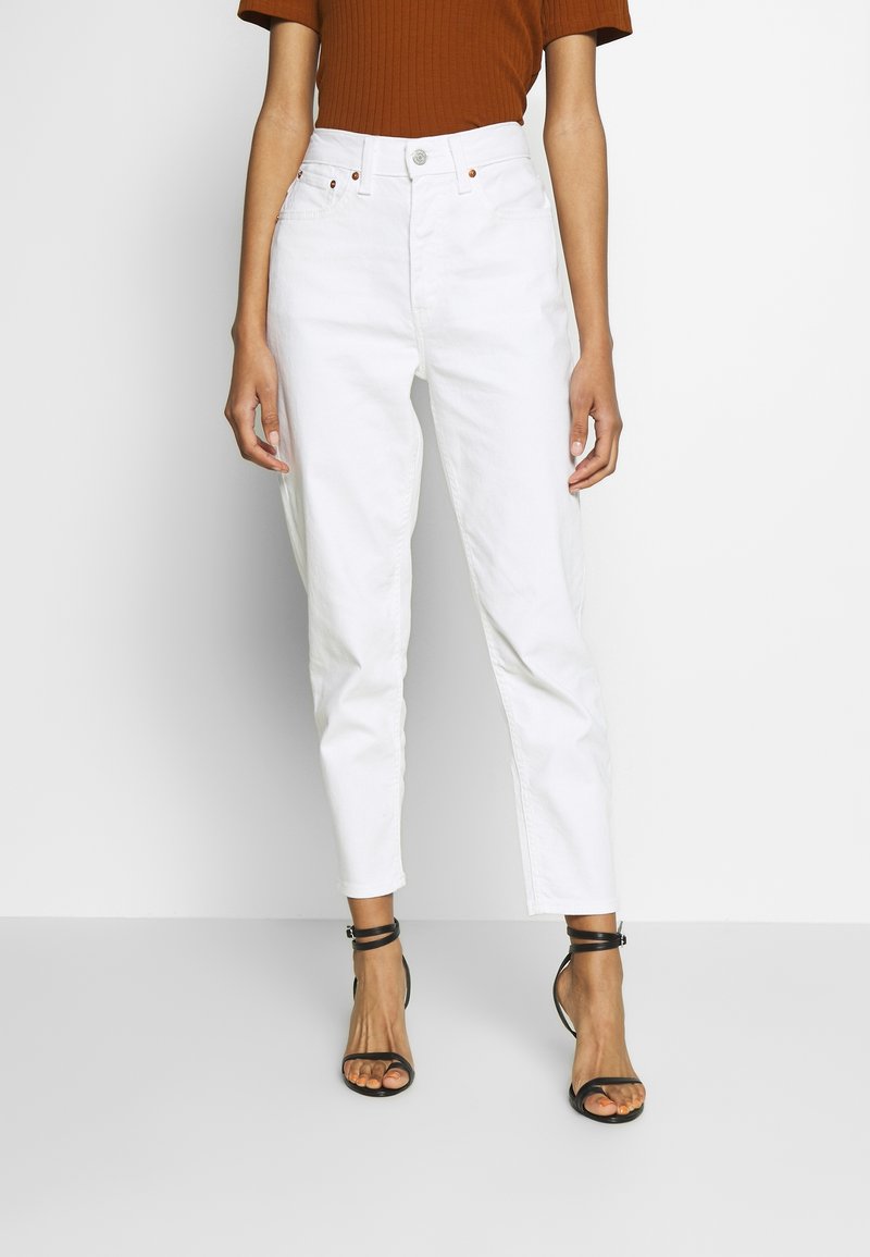 Vita högmidjade jeans med en avsmalnande silhuett, med en frontknäppning och fem fickor. Matchat med en randig brun top och svarta sandaler.