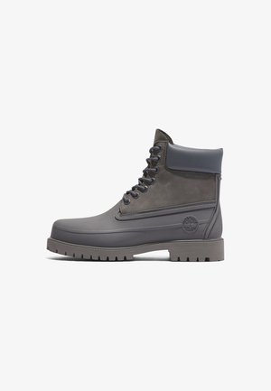 Bota gris impermeable hasta el tobillo con cordones, cuello acolchado y suela resistente, con el logotipo de Timberland en relieve en el lateral.