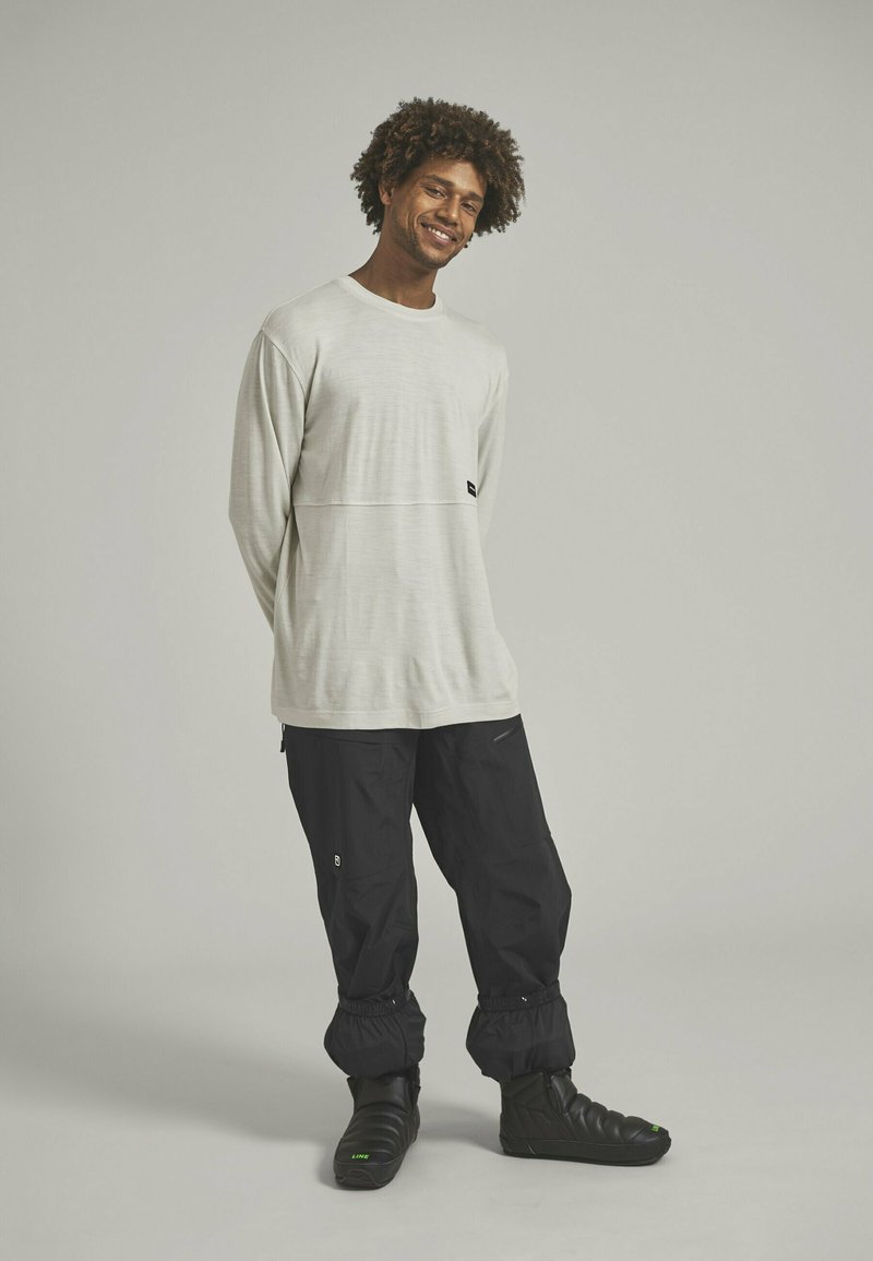 Hellgraues Langarmshirt mit horizontaler Naht, schwarze Cargo-Hosen mit elastischen Bündchen und schwarze Schuhe mit grünen Akzenten.