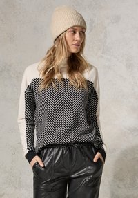 Maglione a righe herringbone in bianco e nero con maniche crema, abbinato a pantaloni in pelle nera larghi e un berretto beige a coste.