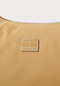 Žuta tkanina s glatkom teksturom, s reljefnim srebrnim pravokutnim logotipom s natpisima "TOMMY" i "JEANS". Jednostavan dizajn, okrugli izrez.
