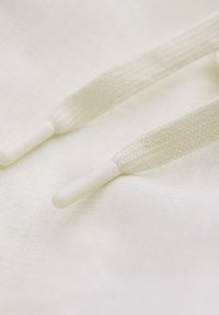 Tissu en coton de couleur écrue avec des cordons texturés tissés et des embouts en plastique blanc, mettant en avant des détails en surface doux et lisses.