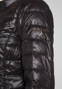 Manche de doudoune matelassée noire brillante avec texte doré "PATRIZIA PEPE" et logo insecte brodés sur le haut du bras.