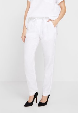 Pantalons en lin blancs à coupe décontractée, avec une taille élastique, des poches latérales et une texture légère, assortis à des escarpins noirs.