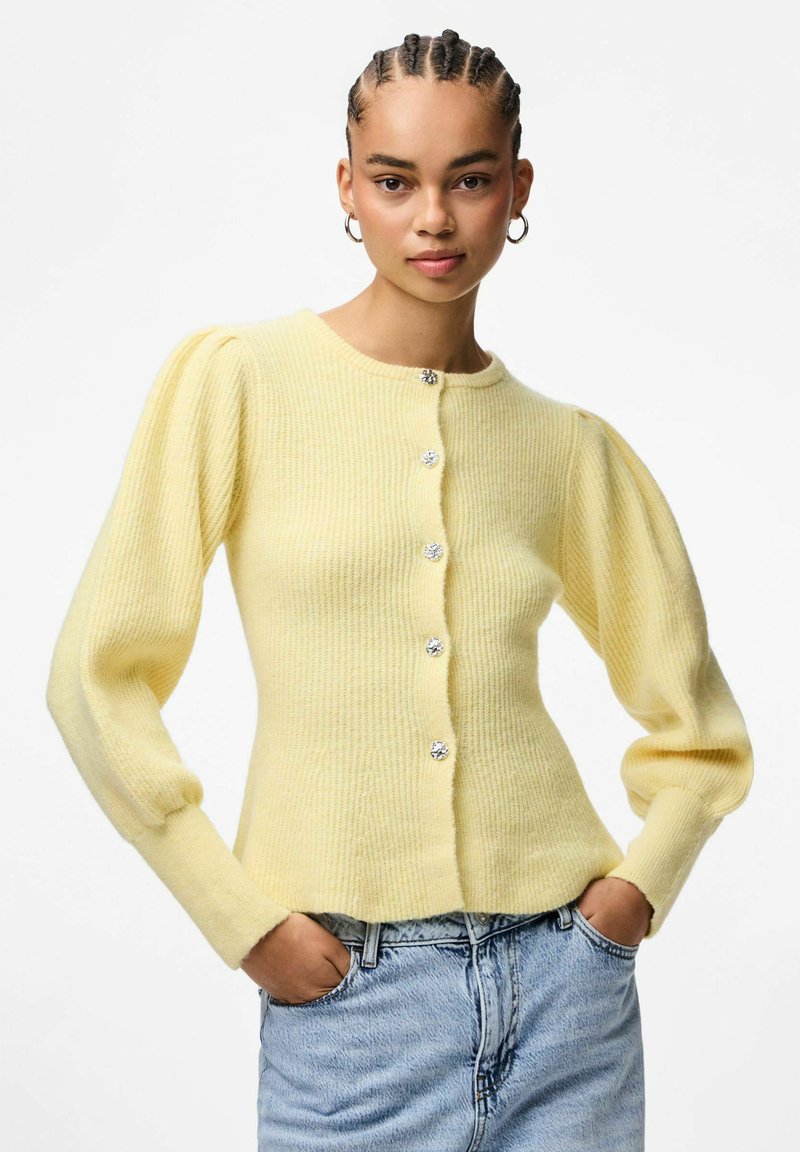 Jasnożółty kardigan w prążki z bufiastymi rękawami, z pięcioma guzikami w kolorze srebrnym z przodu. Miękka tekstura i dopasowany krój w talii.