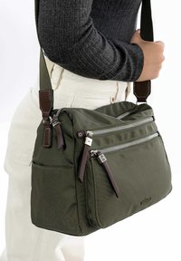 Borsa a spalla verde oliva realizzata in tessuto resistente, con più scomparti con zip e dettagli in pelle marrone.