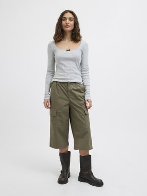 Woman standing, wearing a light gray long-sleeve top, olive green wide-leg cargo pants, and black mid-calf boots against a white background.