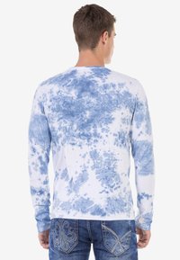 Langärmliges weißes Hemd mit blauer Batikmusterung, Rundhalsausschnitt und lässiger Passform. Die Rückseite zeigt ein weiches, strukturiertes Design.